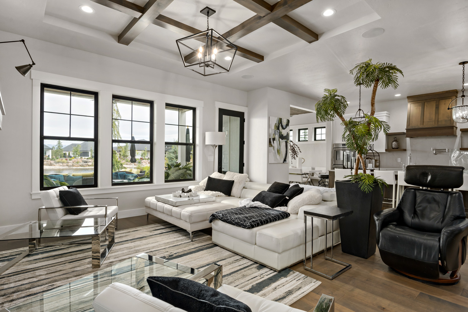 Contemporary living room interior with coffered beam ceiling, black-framed windows, and open kitchen