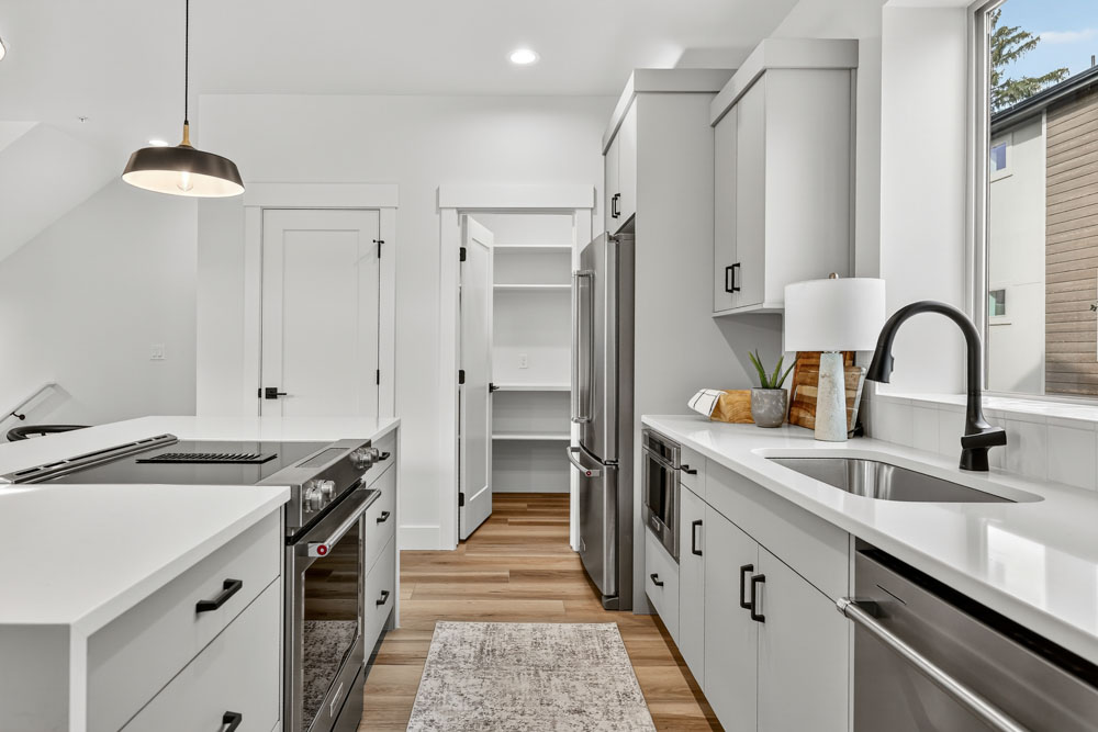 Modern galley kitchen interior with gray cabinets, stainless steel appliances, and white quartz countertops