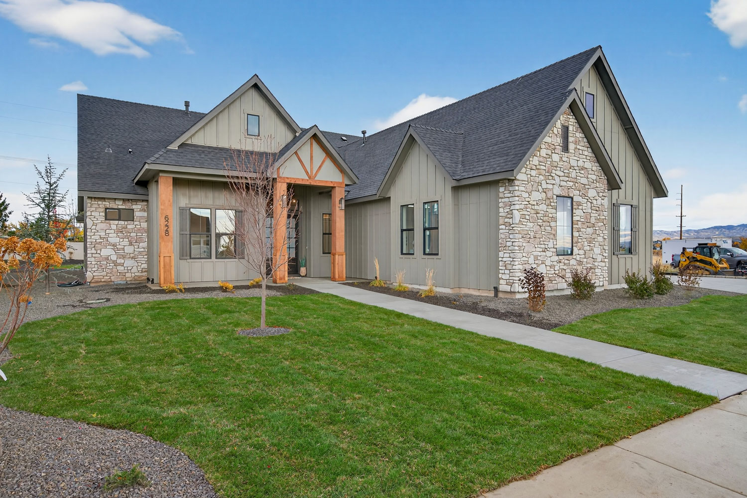 Front exterior of modern farmhouse home with gray board-and-batten siding, natural stone accents, timber-framed entry porch, and landscaped walkway