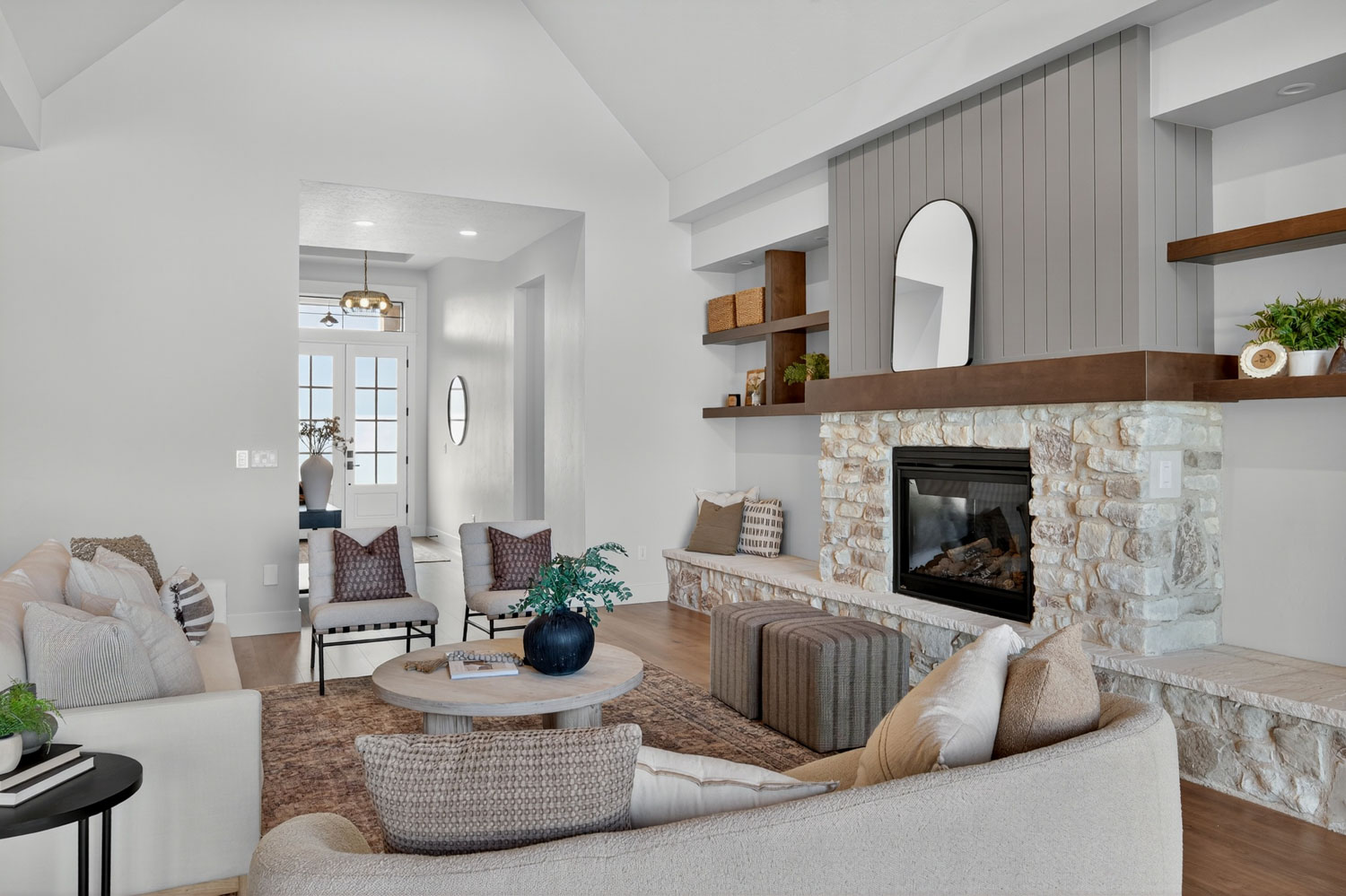 Modern farmhouse living room with stone fireplace, shiplap accent wall, floating wood shelves, and neutral furniture on hardwood floors