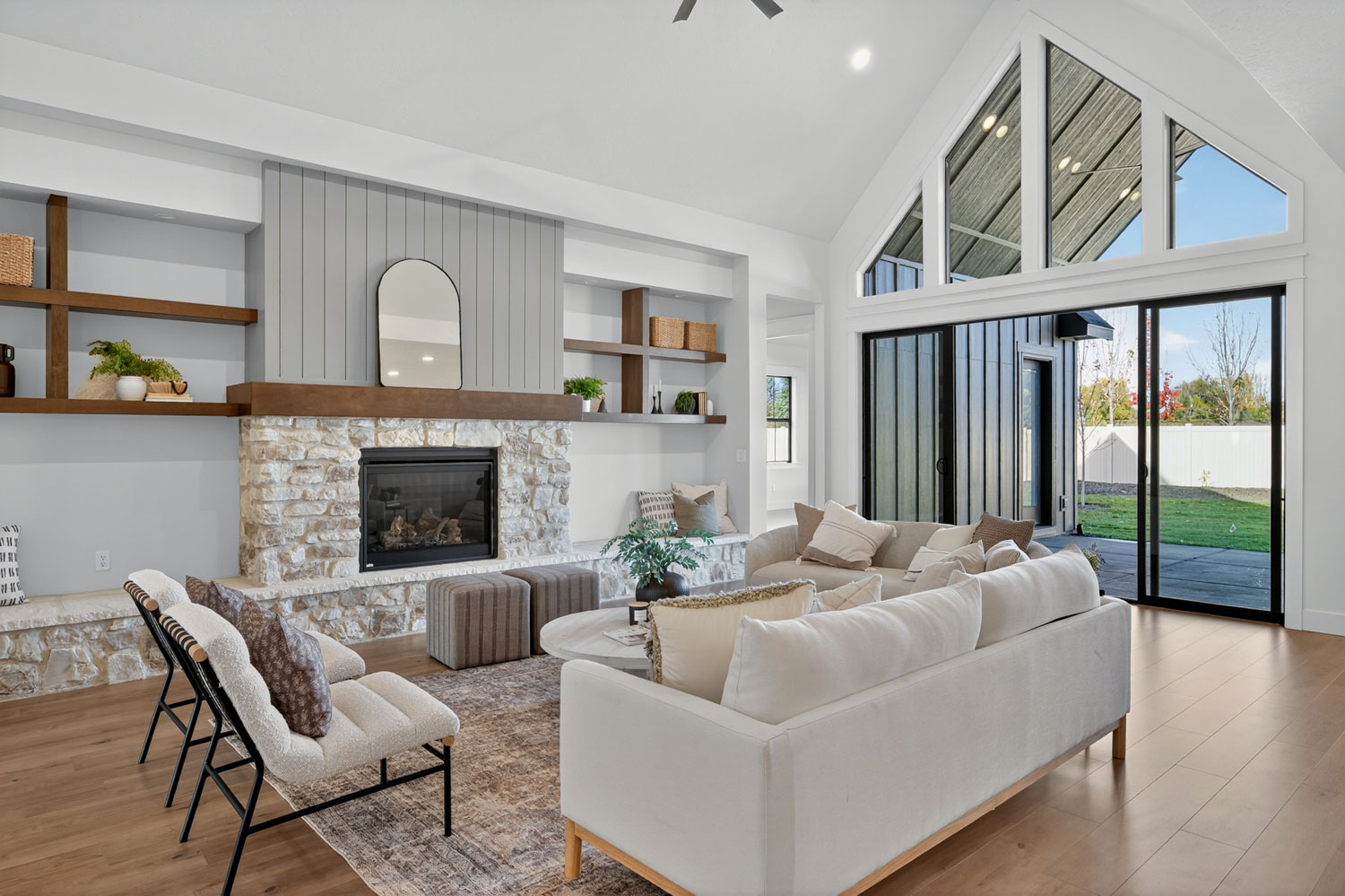 Living room with vaulted ceilings, stone fireplace, built-in shelving, and floor-to-ceiling folding glass patio doors