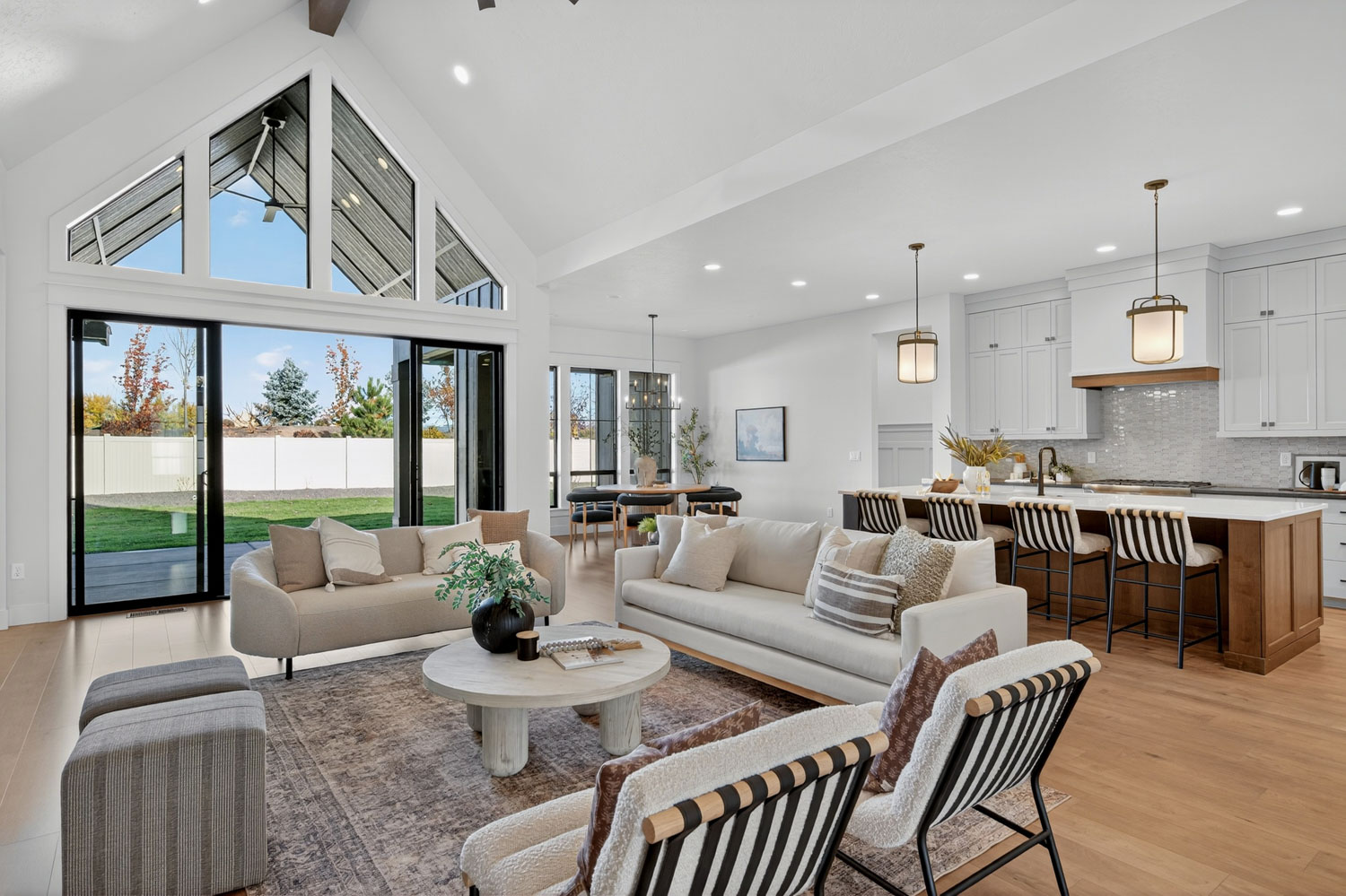 Open floor plan living area with cathedral ceiling glass wall, neutral sofas, and seamless flow into kitchen with island seating
