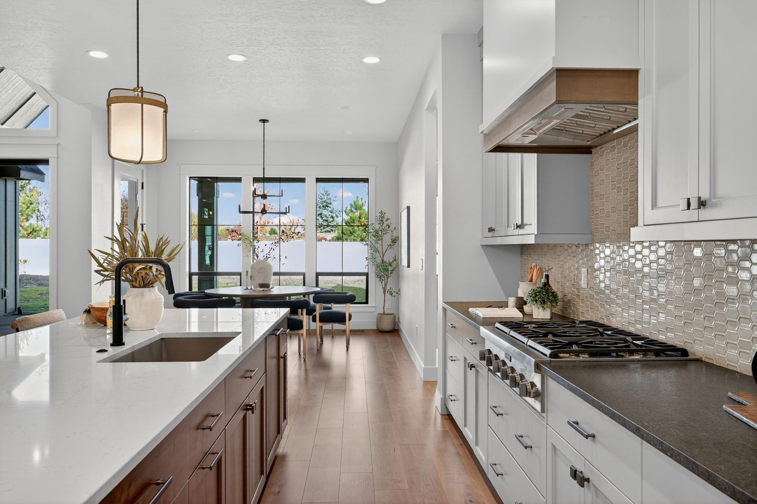 Modern farmhouse kitchen with white quartz island, wood base cabinets, hexagon tile backsplash, gas range, and pendant lighting