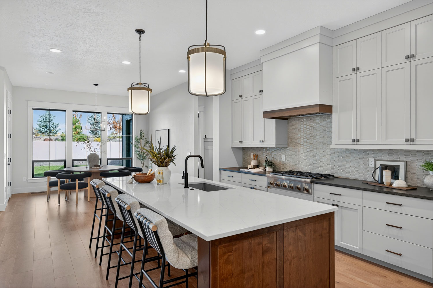 Gourmet kitchen with large wood island, quartz countertop, striped bar stools, white shaker cabinets, and pendant lights