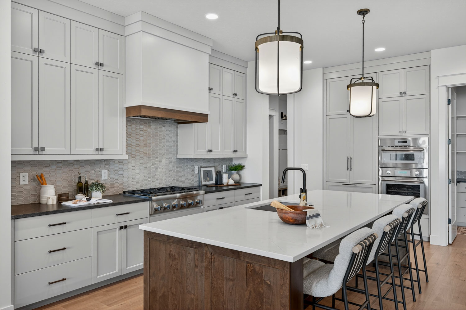 Custom kitchen with white shaker cabinets, wood-trimmed range hood, hexagon tile backsplash, stained wood island, and stainless appliances