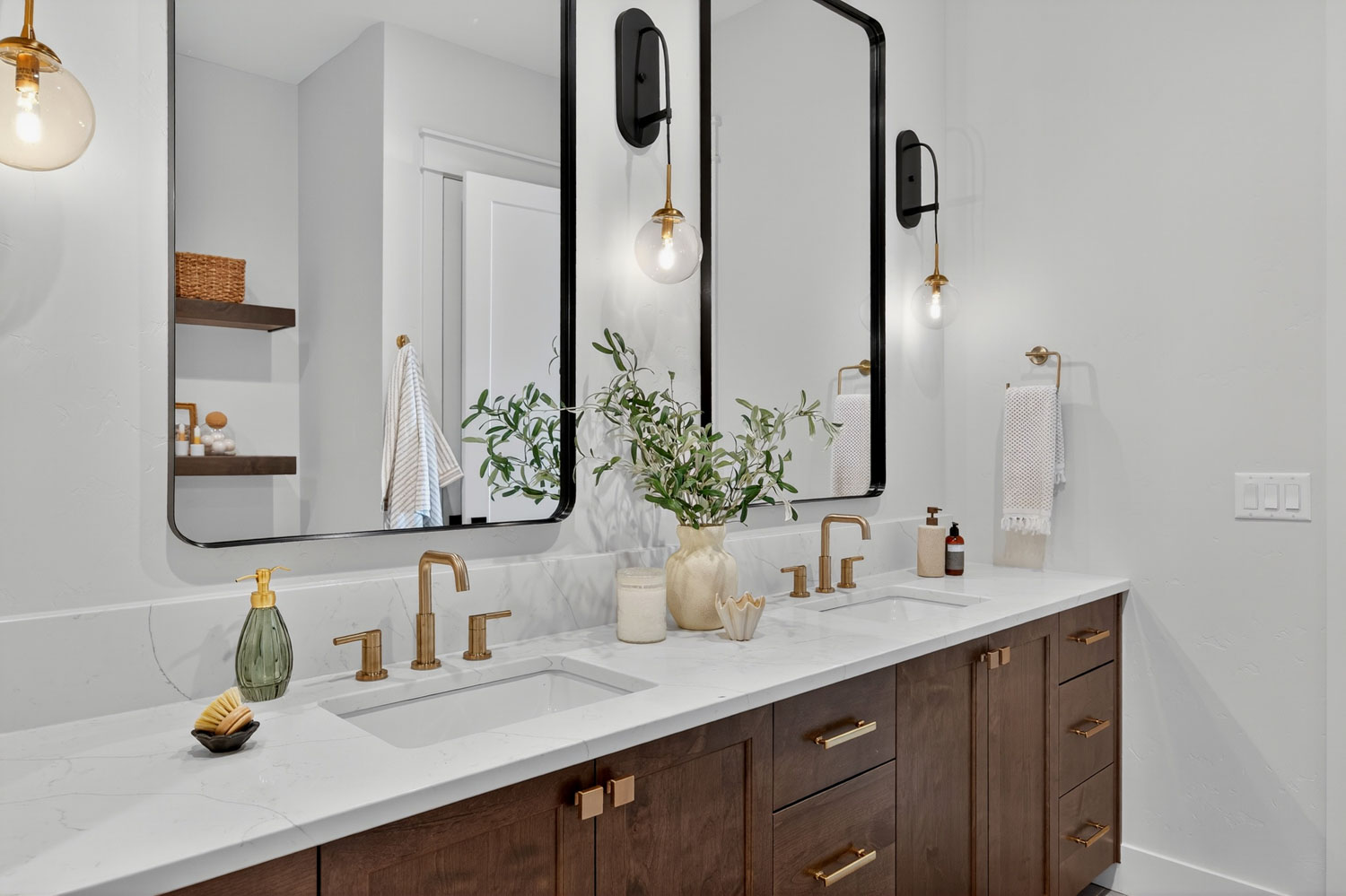 Modern double vanity bathroom with dark wood cabinetry, white quartz countertops, brushed gold faucets, and globe wall sconces