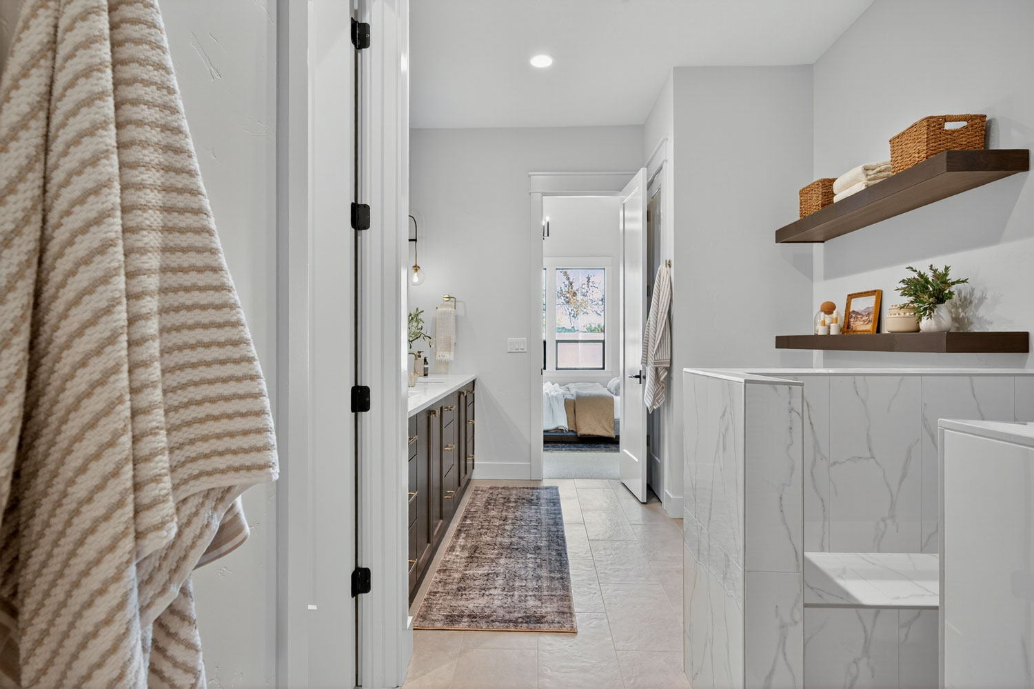 Master bathroom with marble-look tile half wall, dark wood floating shelves with wicker storage baskets, and vanity area
