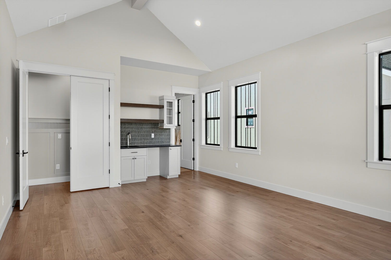 Spacious bonus room with vaulted ceilings, hardwood flooring, built-in wet bar, and multiple black-framed windows