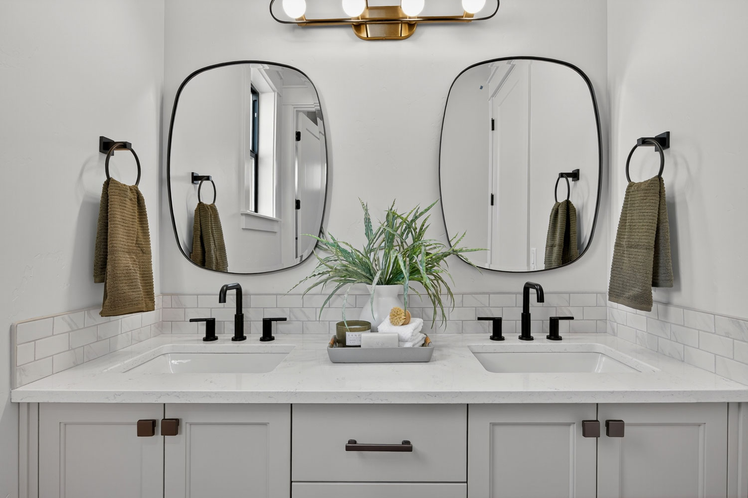 Double vanity bathroom with light gray shaker cabinets, white quartz countertops, matte black fixtures, and organic-shaped mirrors