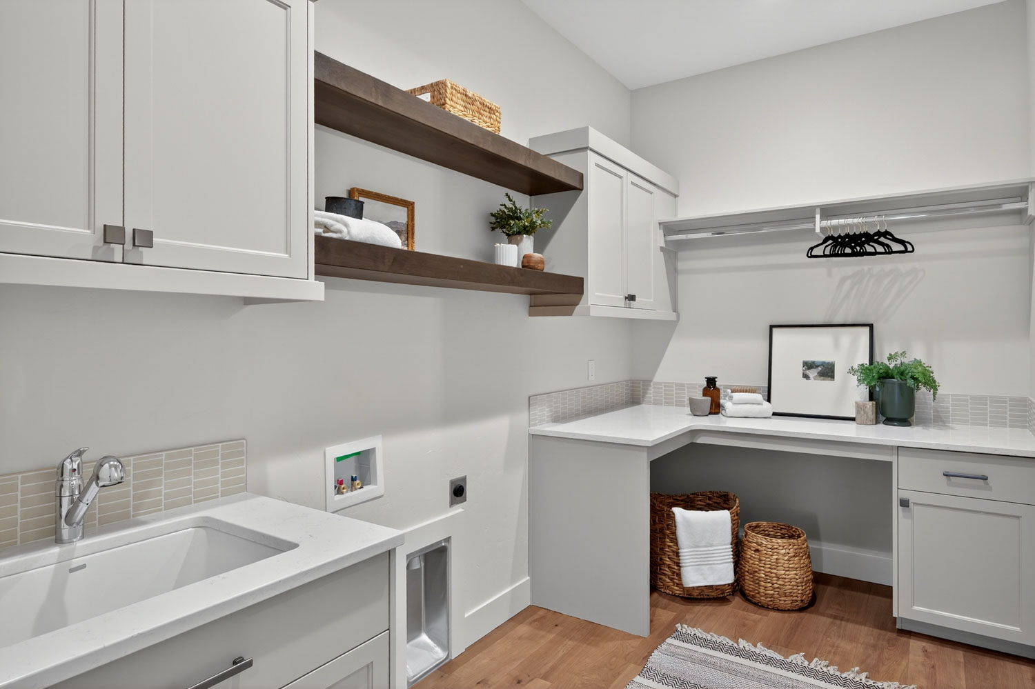 Laundry room with white shaker cabinets, dark wood floating shelves, quartz countertop utility sink, and folding station