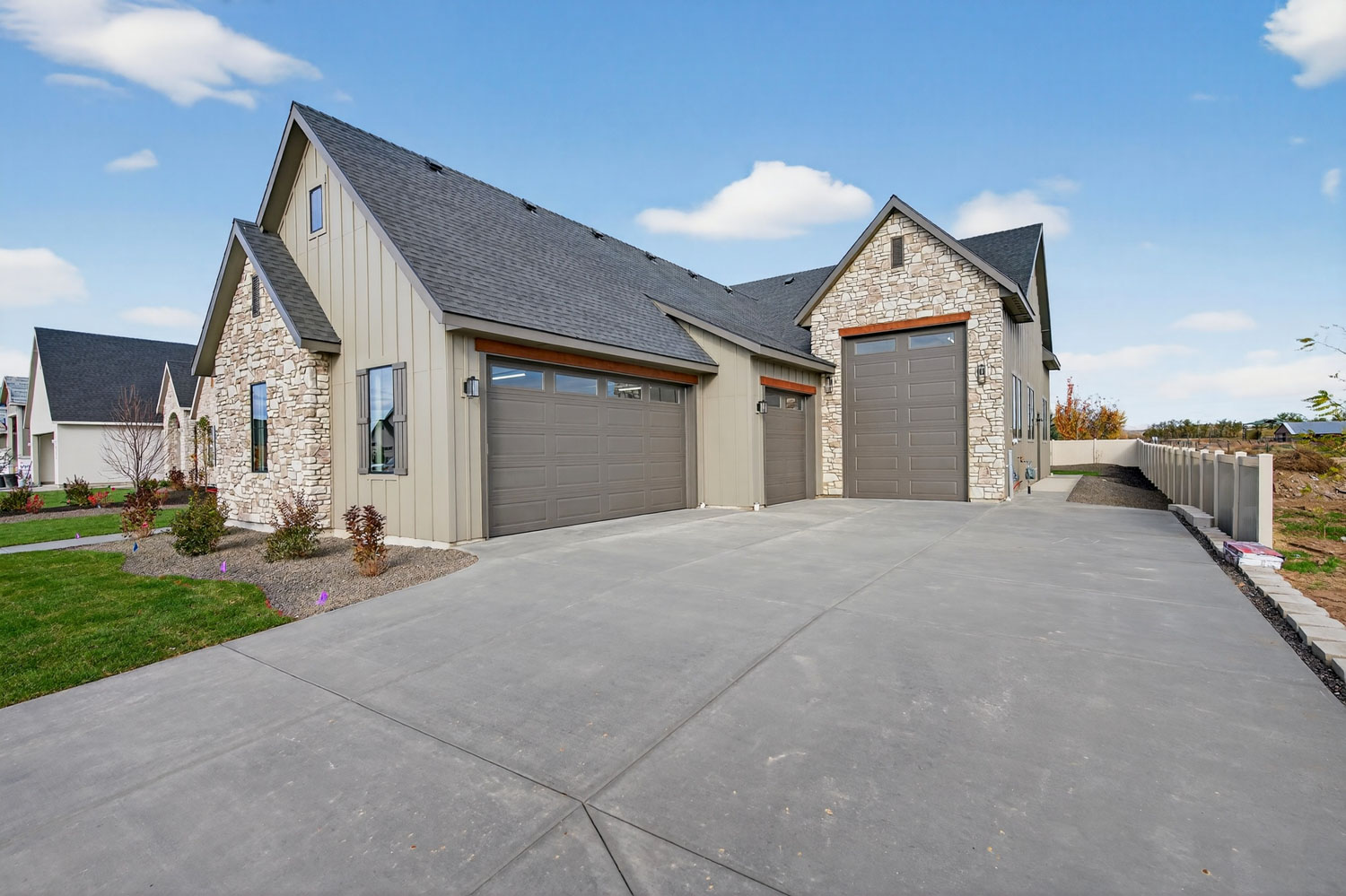 Modern farmhouse exterior with stone and board-and-batten siding, three-car garage, wide driveway, and professional landscaping