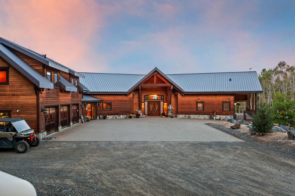 Exterior twilight view of luxury log home with metal roof and paver driveway near Boise Idaho