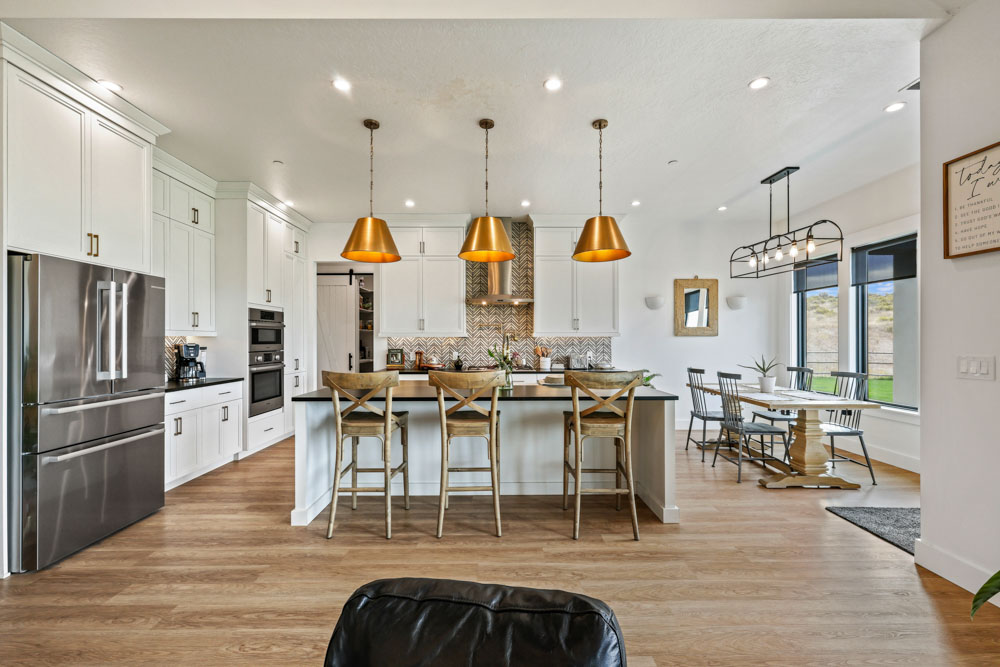 Open-concept interior kitchen with white cabinets, gold pendants, and dining area in Boise Idaho