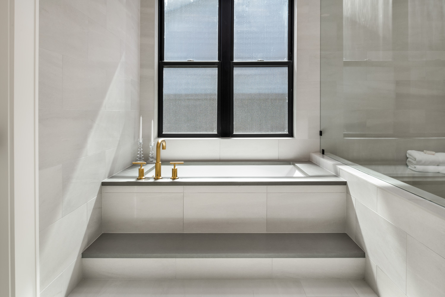 Modern interior master bathroom with soaking tub, gold fixtures, and black-framed window