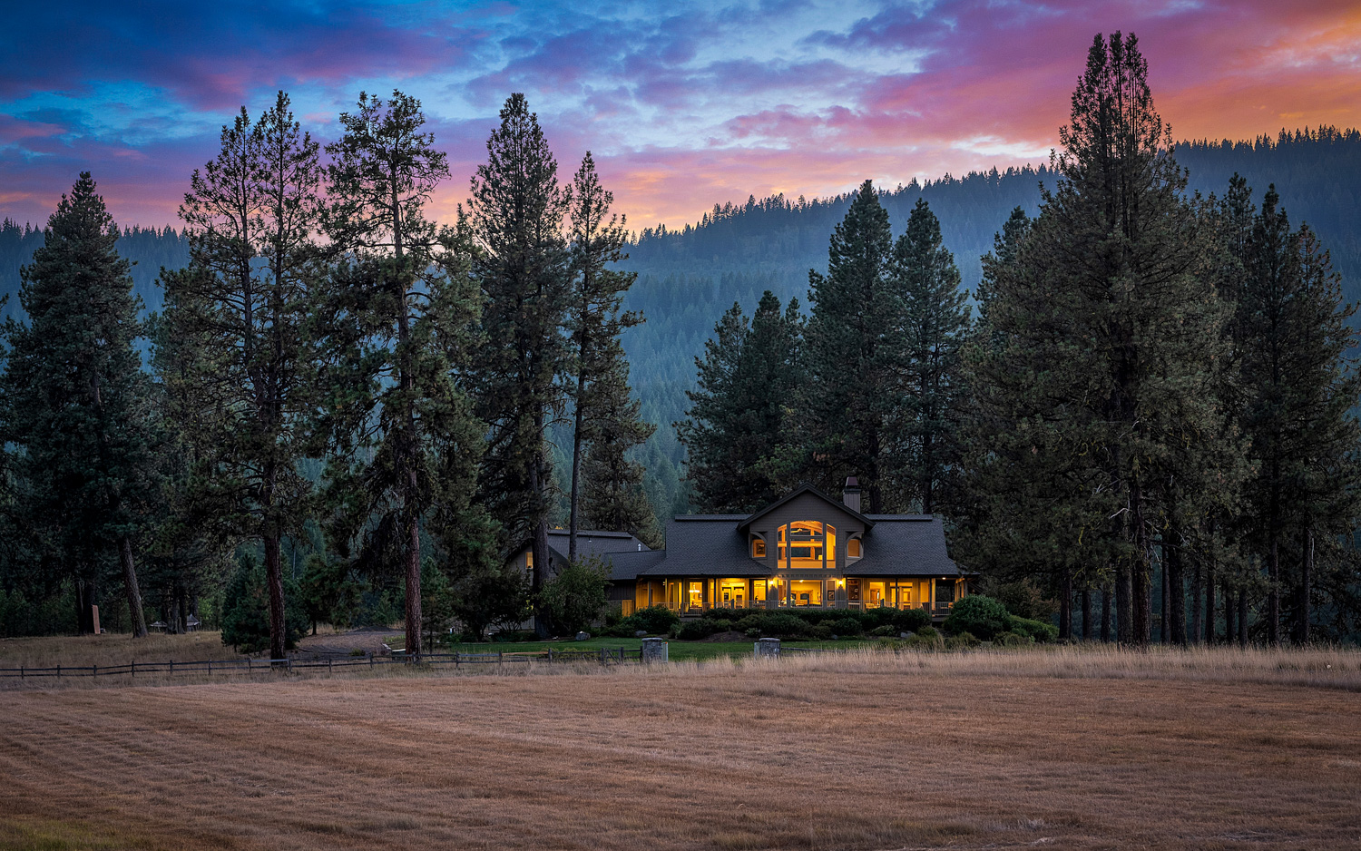 Twilight exterior of luxury home surrounded by tall pine trees in Boise Idaho