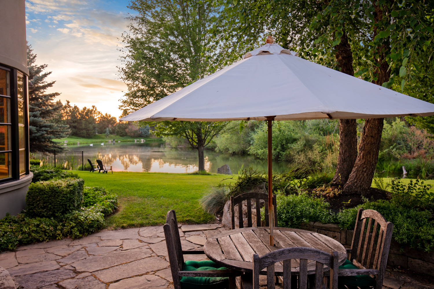 Outdoor patio with umbrella and Adirondack chairs overlooking lawn at sunset in Boise