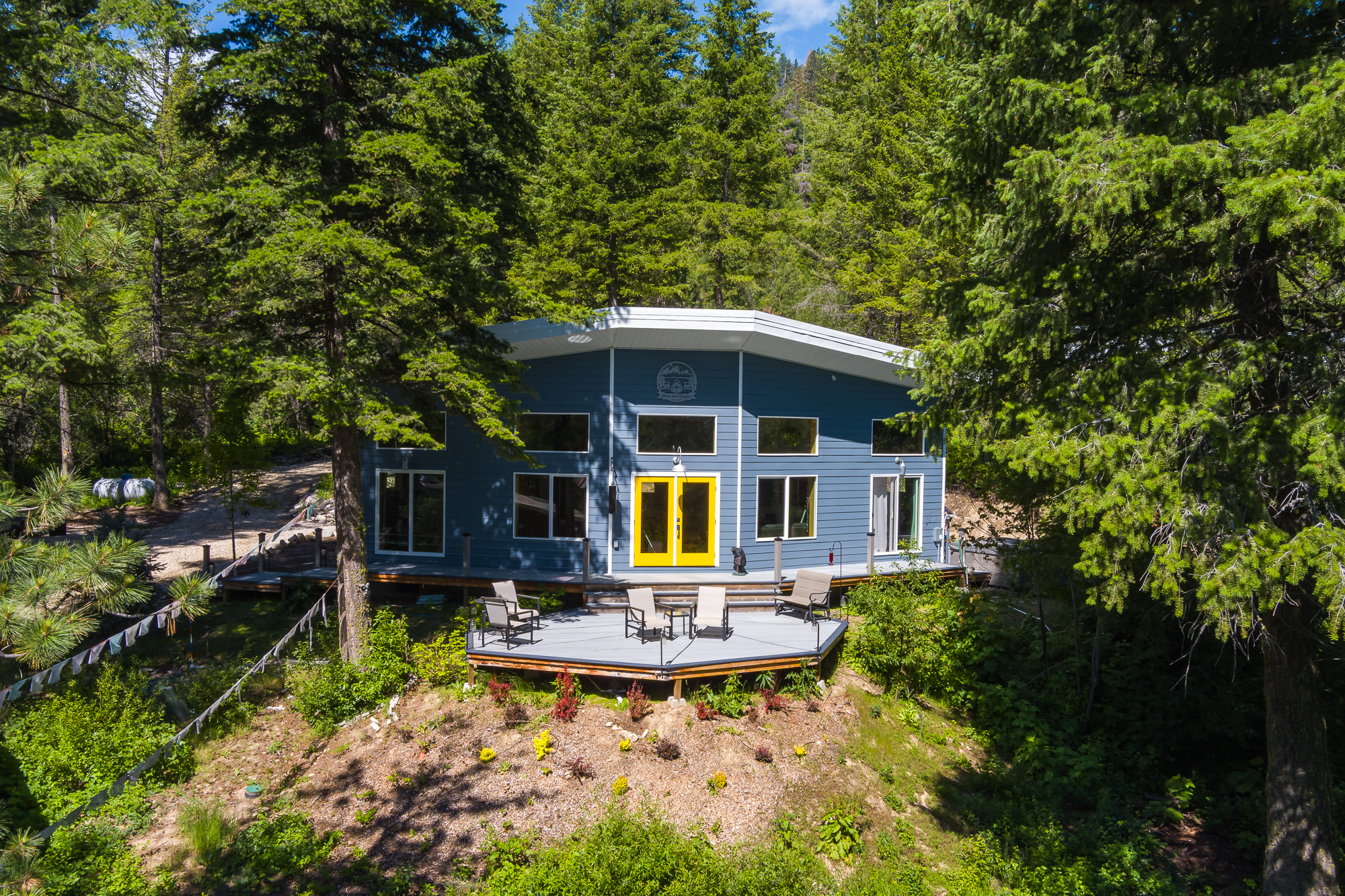 Aerial view of blue modern cabin with large deck surrounded by Idaho forest