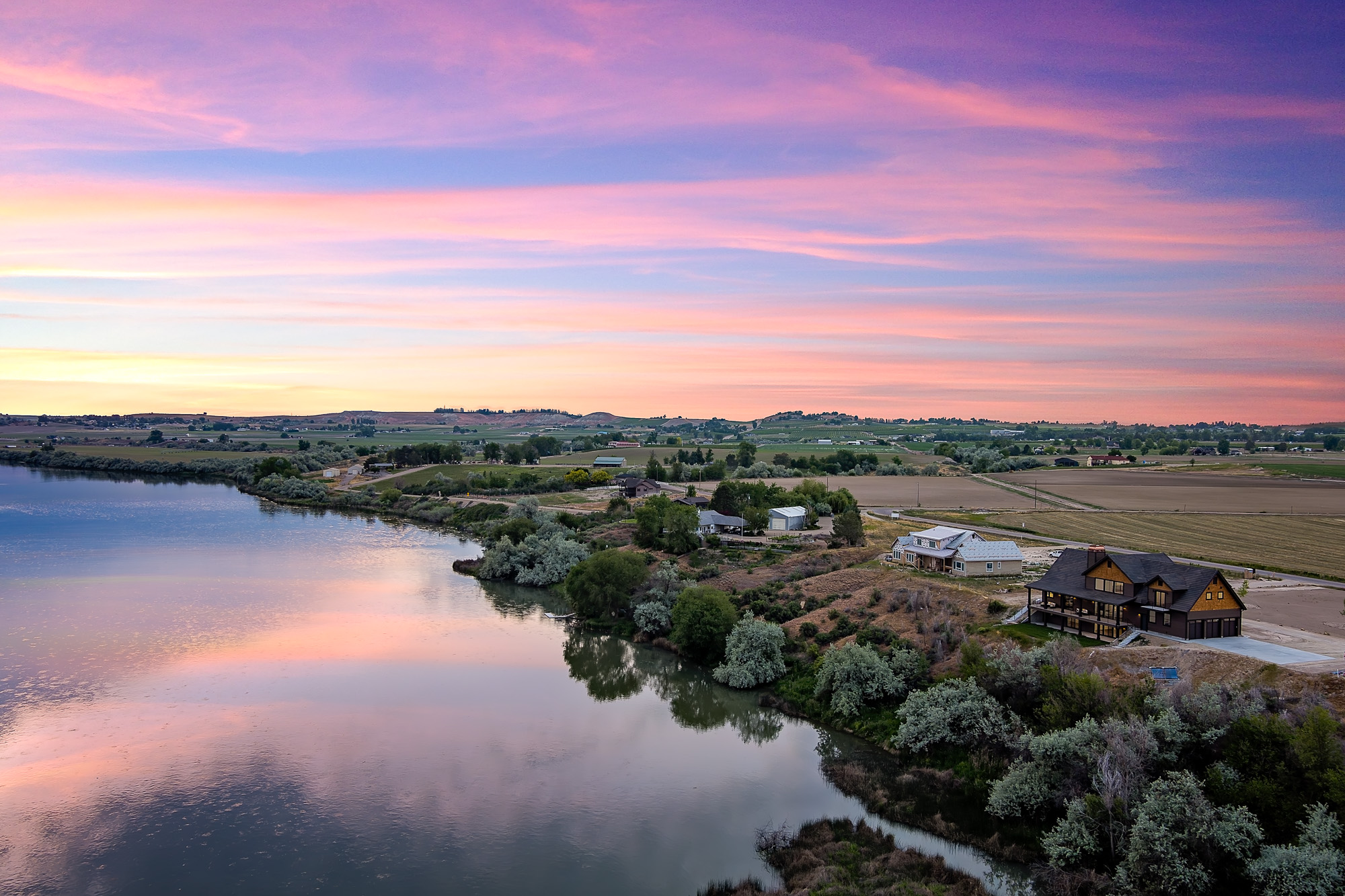 Aerial drone view of riverfront home on Idaho river bend with farmland and sunset reflections