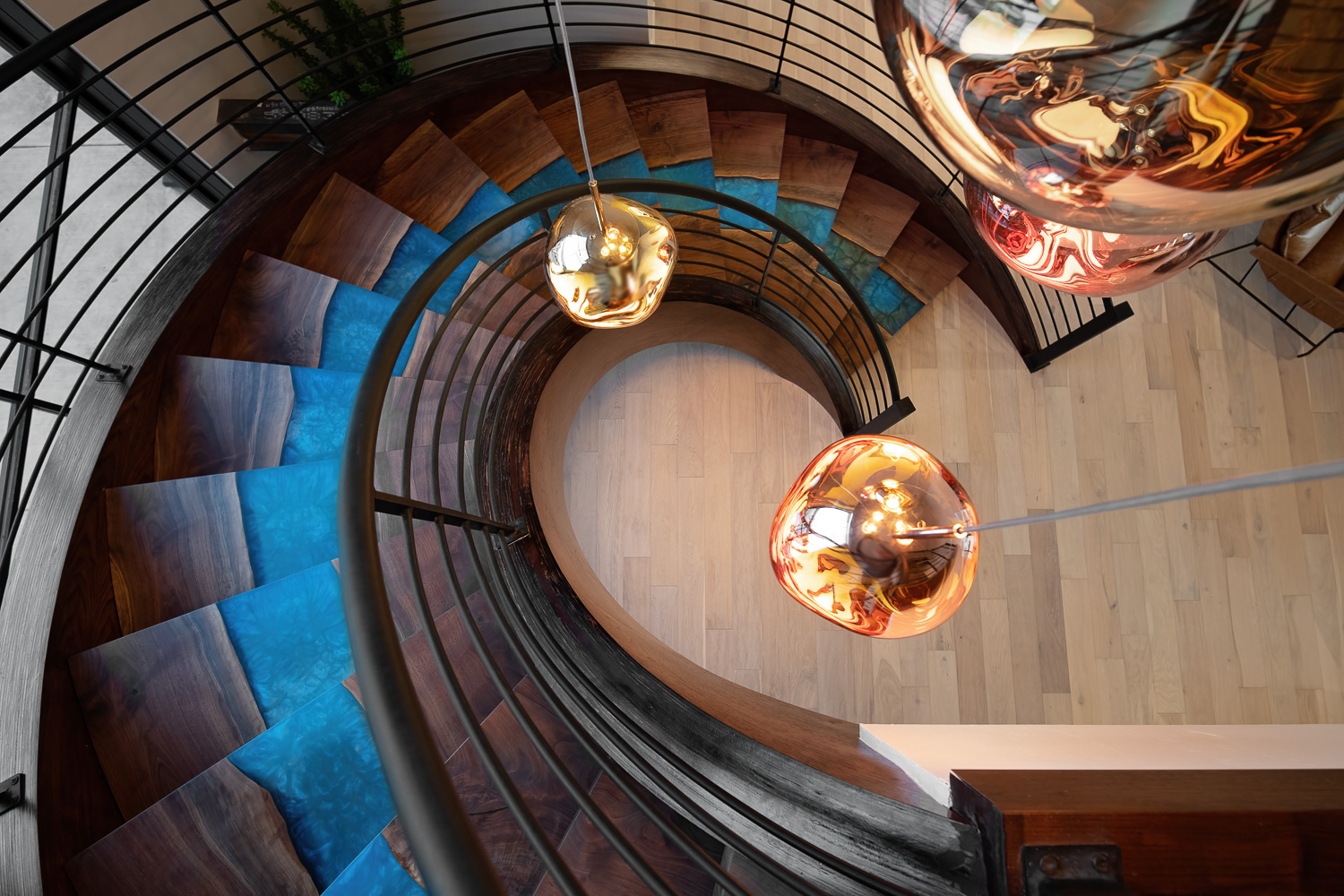 Luxury interior spiral staircase with walnut steps, blue epoxy risers, and gold pendant lights
