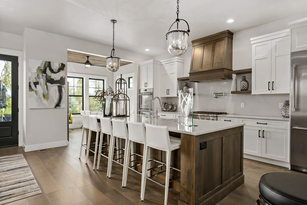 Interior gourmet kitchen with white cabinets, wood range hood, and quartz island in Boise home