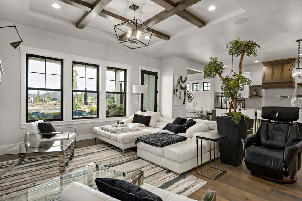 Contemporary living room interior with coffered beam ceiling, black-framed windows, and open kitchen
