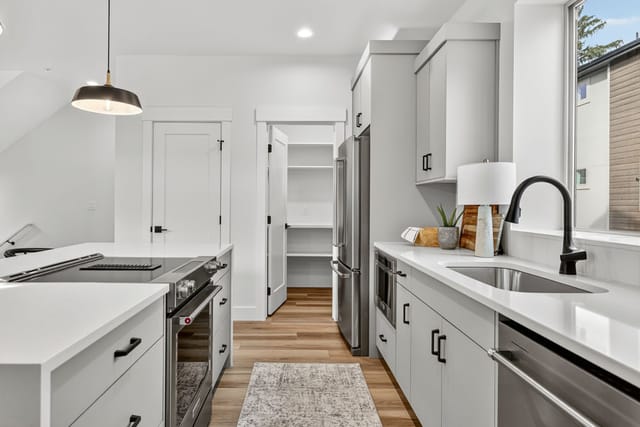 Modern galley kitchen interior with gray cabinets, stainless steel appliances, and white quartz countertops