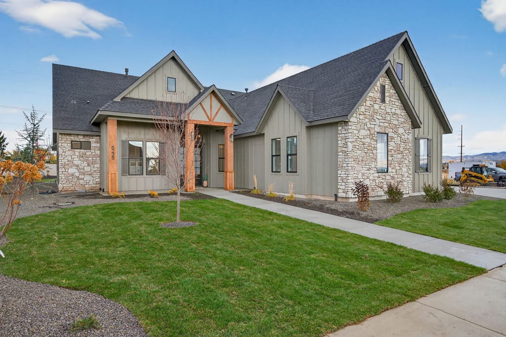 Front exterior of modern farmhouse home with gray board-and-batten siding, natural stone accents, timber-framed entry porch, and landscaped walkway