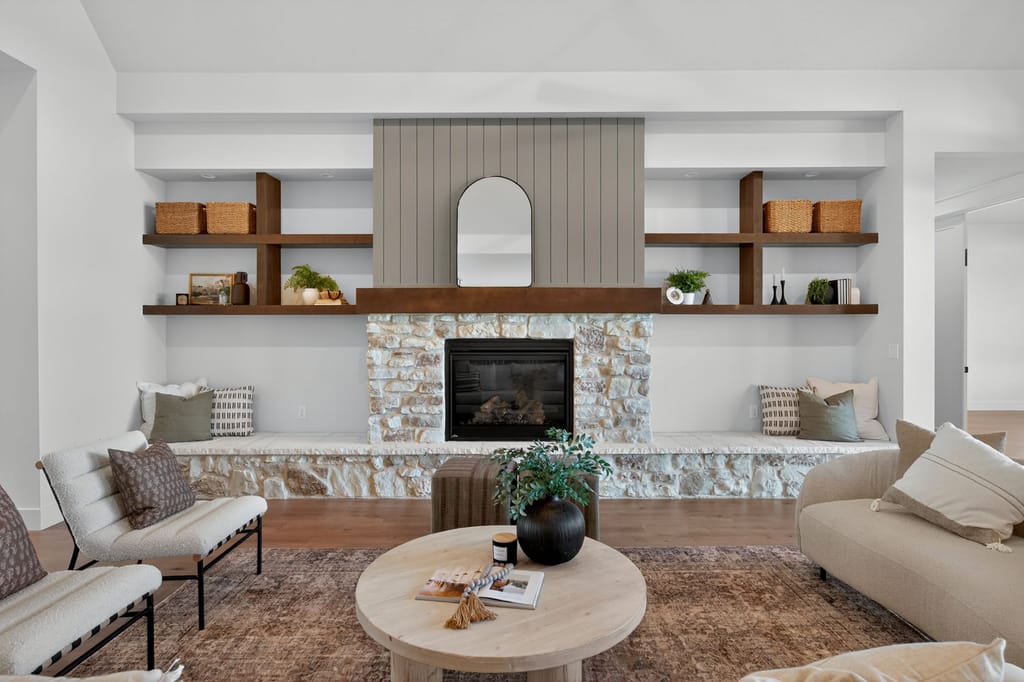 Stone fireplace feature wall with shiplap paneling, arched mirror, floating wood shelves with woven baskets, and neutral seating