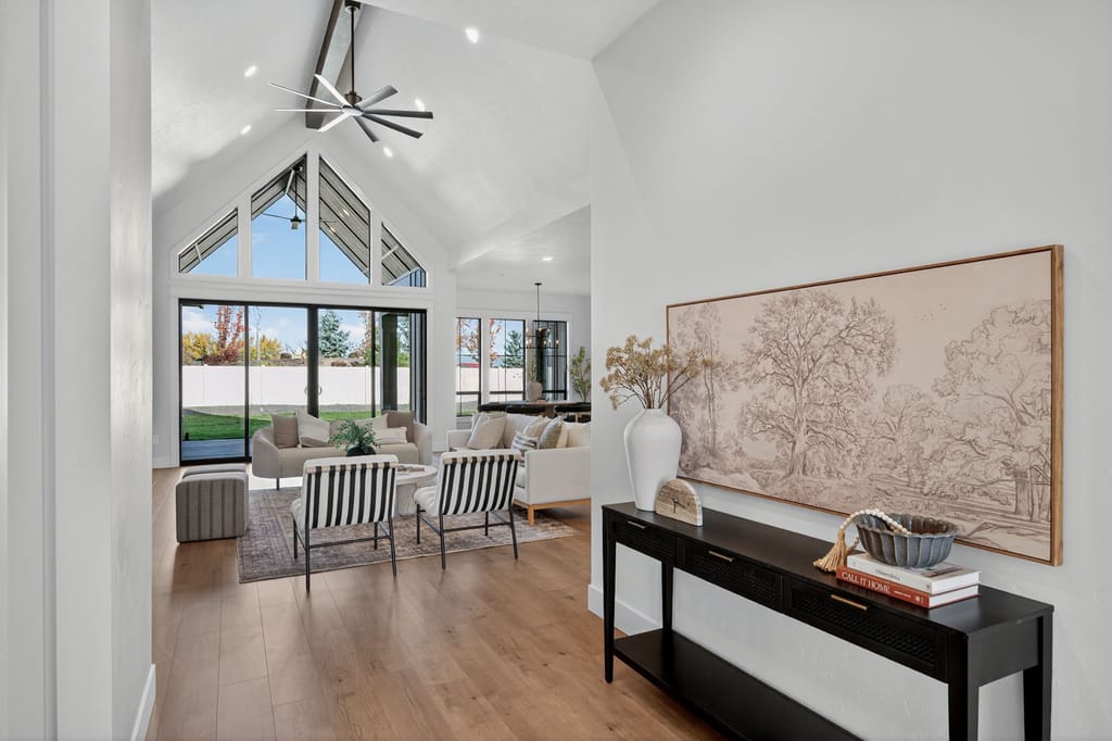Open entryway with vaulted peaked windows, black-framed sliding glass doors, striped accent chairs, and framed artwork