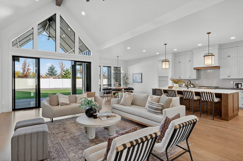Open floor plan living area with cathedral ceiling glass wall, neutral sofas, and seamless flow into kitchen with island seating