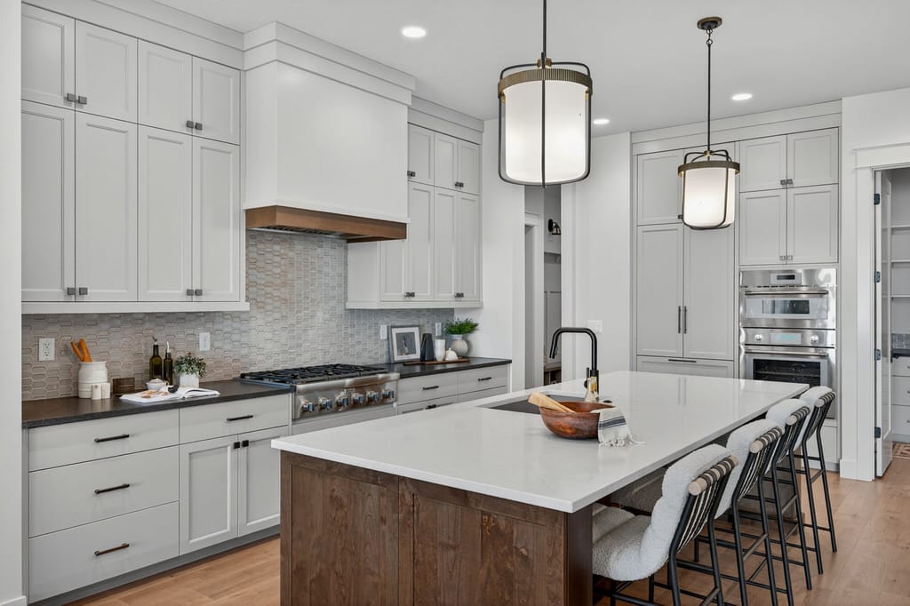 Custom kitchen with white shaker cabinets, wood-trimmed range hood, hexagon tile backsplash, stained wood island, and stainless appliances