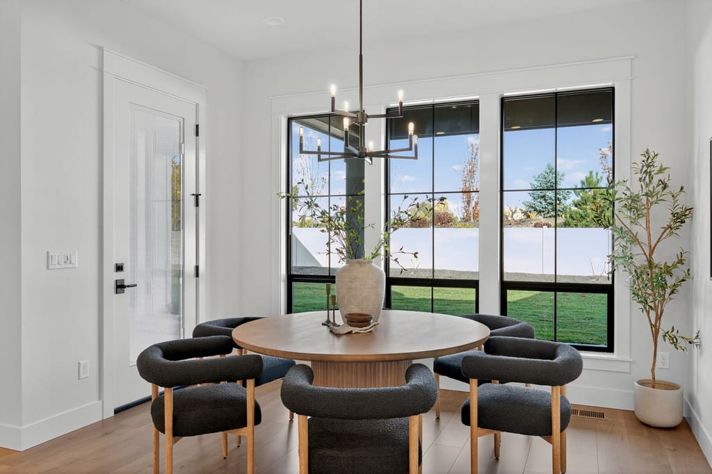 Breakfast nook with round wood dining table, dark boucle chairs, modern chandelier, and large windows overlooking the backyard
