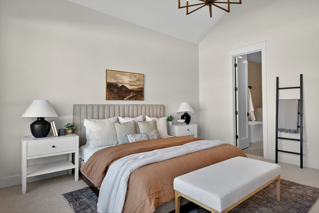 Master bedroom with vaulted ceiling, channel-tufted headboard, warm terracotta bedding, white nightstands, and gold chandelier