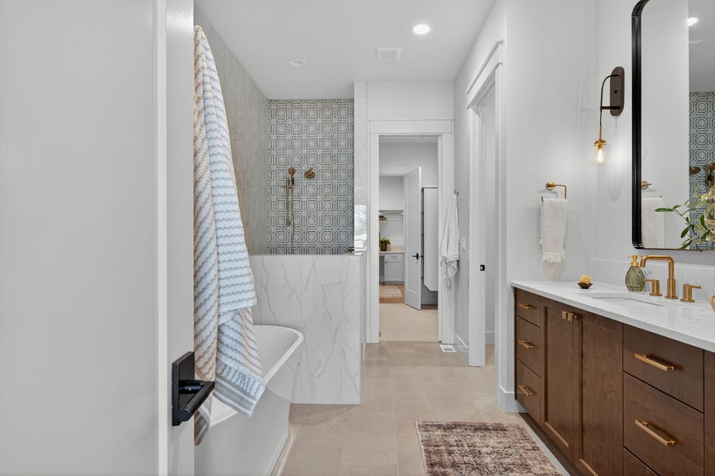 Luxurious master bathroom with freestanding soaking tub, geometric patterned accent tile shower, and dark wood vanity with gold hardware