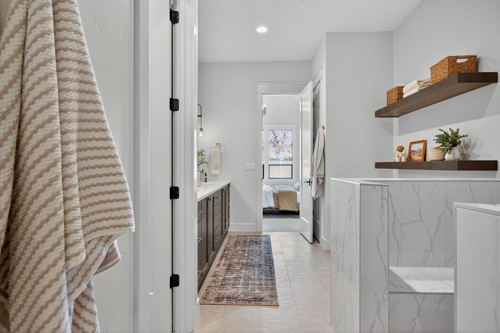 Master bathroom with marble-look tile half wall, dark wood floating shelves with wicker storage baskets, and vanity area