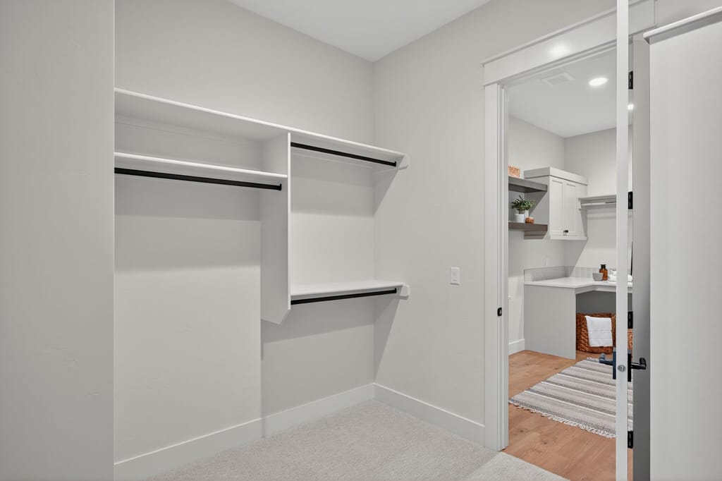 Spacious walk-in closet with built-in white shelving, black hanging rods, and direct access to laundry room