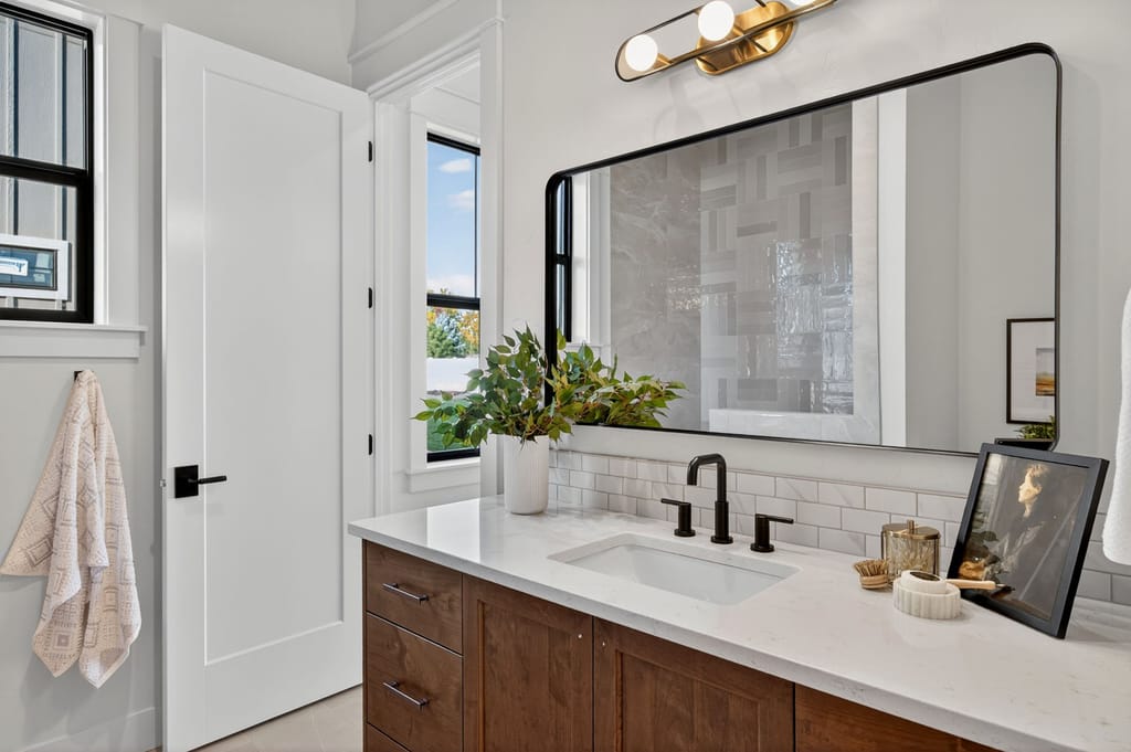 Guest bathroom vanity with wood cabinetry, white quartz countertop, matte black faucet, subway tile, and brass vanity light