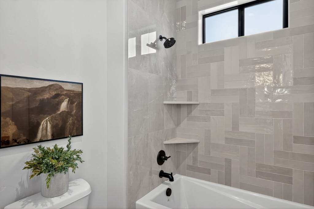 Guest bathroom tub-shower with gray herringbone accent tile wall, matte black fixtures, and transom window for natural light