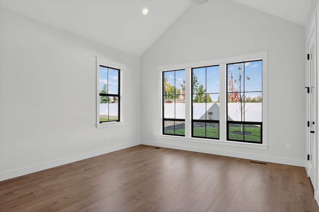 Bright bonus room with vaulted ceiling, hardwood floors, large black-framed grid windows, and natural light