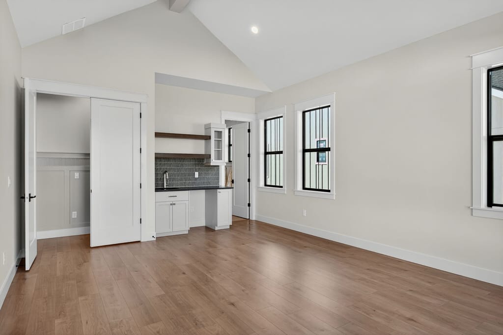 Spacious bonus room with vaulted ceilings, hardwood flooring, built-in wet bar, and multiple black-framed windows