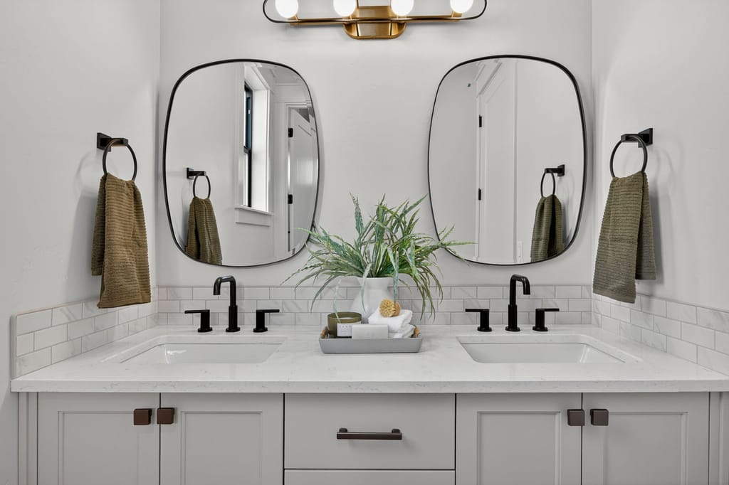 Double vanity bathroom with light gray shaker cabinets, white quartz countertops, matte black fixtures, and organic-shaped mirrors