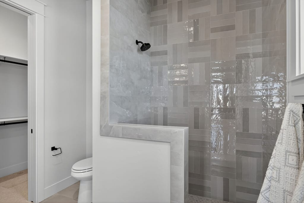 Walk-in shower with glossy gray herringbone accent tile wall, half-wall partition, and matte black showerhead