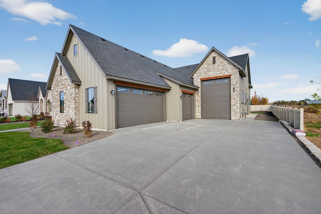 Modern farmhouse exterior with stone and board-and-batten siding, three-car garage, wide driveway, and professional landscaping
