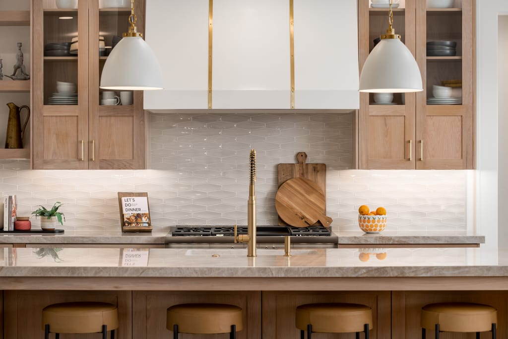 Interior kitchen with oak cabinets, marble countertops, gold fixtures, and hexagonal tile backsplash