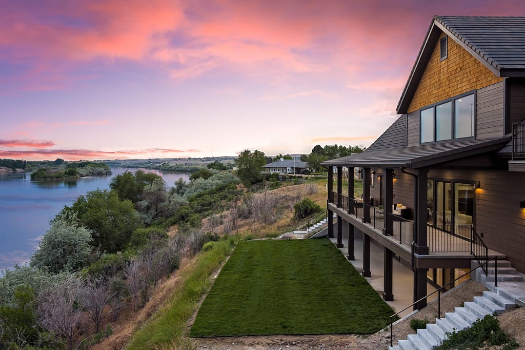 Craftsman riverfront home with wraparound deck overlooking Idaho river at sunset