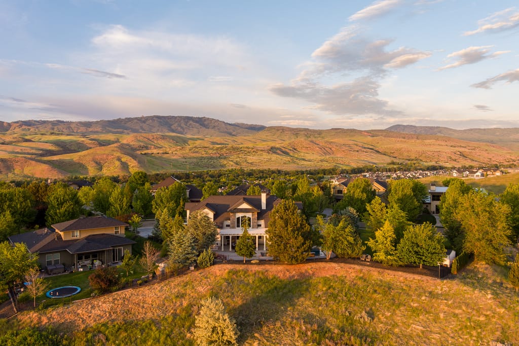 Aerial view of two-story home with stone accents among trees in Idaho foothills at golden hour
